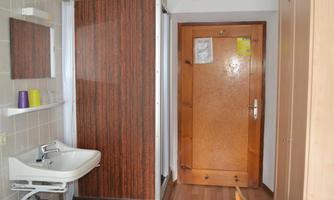 A bathroom with a shower cabin, a sink, and a large wooden door. The floor has a wood look and the walls are tiled.