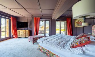 A stylish bedroom with colorful accents and large windows. The atmosphere is cozy and inviting, with an elegant bed and decorative curtains.