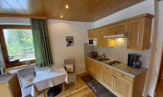A bright kitchen with wooden cabinets and a small dining area. The view of the greenery outside the window creates an inviting atmosphere.