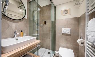 A modern bathroom with a shower and a white sink. The walls are in neutral tones, and there is a large wall mirror.