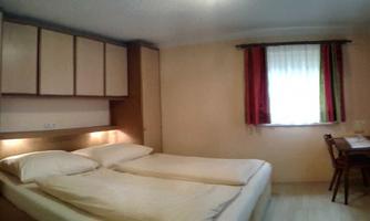 A simple room with two single beds and a desk. Bright walls and large windows create a pleasant atmosphere.