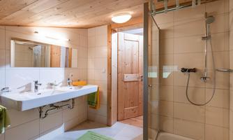 A modern bathroom with a wooden ceiling and bright tiles. The shower is glazed and there is a large sink with a mirror.