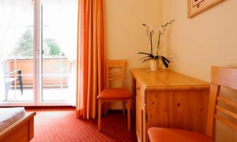 A bright room with wooden furniture and orange chairs.  
Large windows with a view of the balcony and a houseplant on the dresser.