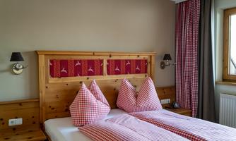 A cozy bedroom with two beds and checkered pillows. The walls are in neutral colors and there is a large windowsill with curtains.