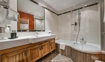 A modern bathroom with a bathtub and a separate shower. The space is bright and stylish, equipped with wooden details and a large mirror.