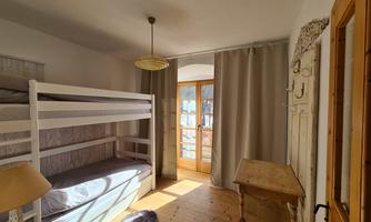 A bright room with a bunk bed and wooden floor. Large windows let in plenty of daylight.