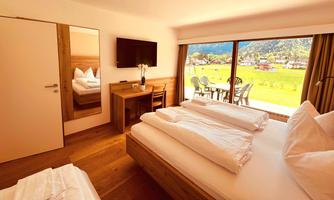 A modern bedroom with hardwood flooring and a large window that offers a view of the landscape. The decor is bright and minimalist, featuring a television and a desk.