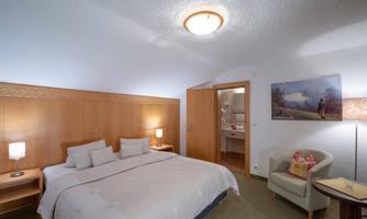 A cozy bedroom with a large bed and wood paneling. The room features a seating area and access to a bathroom.