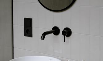 A modern bathroom with a round mirror and an elegant wash basin. The black fittings and minimalist decoration give the space a stylish look.