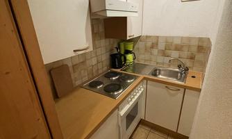A small kitchen with white cabinets and wooden surfaces. There is a stove, a sink, and some kitchen appliances on the countertop.