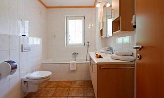 A modern bathroom with a bathtub, a sink, and bright tiles. There are large windows and wooden cabinets for extra storage space.