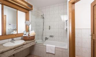 A modern bathroom with a bathtub and a shower. It has bright tiles and a solid wood shelf for towels.