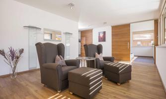 A modernly furnished living space with comfortable armchairs and a coffee table. The large windows bring plenty of light into the room and showcase the wooden floors.