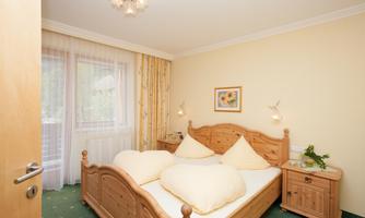 A cozy bedroom with a double bed and bright, cheerful colors. The room has a large window and wooden shelves for extra storage space.