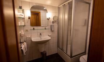 A modern bathroom with a shower and a sink. The walls are tiled and there is bright lighting.