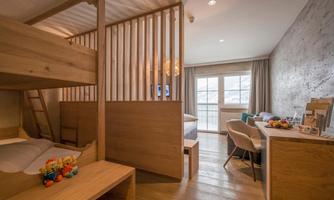 A modern bedroom with a wooden loft bed and a bright, cozy atmosphere. The room has large windows that let in plenty of daylight.
