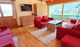 A cozy living area with red sofas and a wooden table. Large windows offer a beautiful view of the landscape.