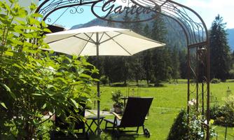 An inviting garden with a sun umbrella and comfortable lounge chairs. In the background, green meadows and trees can be seen, creating a tranquil atmosphere.