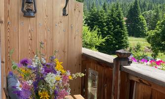 A cozy balcony with a wooden table and a bouquet of flowers. In the background, green mountains and blue sky can be seen.