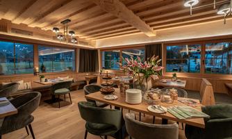 A cozy restaurant with wooden walls and large windows. The tables are stylishly set and decorated with fresh flowers.