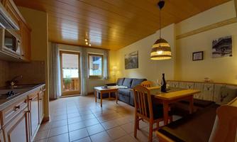 A cozy apartment with modern furniture and wooden ceiling. It features an integrated kitchen, a dining area, and plenty of natural light.