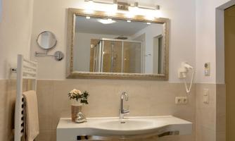 A modern bathroom with an elegant sink and a large mirror. The walls are light and there is a shower in the background.