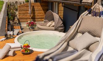 A beautifully decorated outdoor area with a hot tub and comfortable loungers. Flowers and a fruit basket create an inviting atmosphere for relaxation.