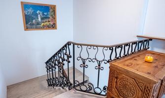 A staircase with a decorative railing and a wooden cabinet. A picture of a landscape hangs on the wall.