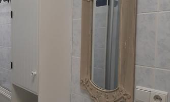 A modern bathroom with a white sink and an elegant framed mirror. The walls are painted in light colors and there is a cabinet for storage.
