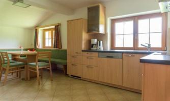 A modern kitchen with wooden cabinets and a cozy seating area. The large windows let in plenty of light.