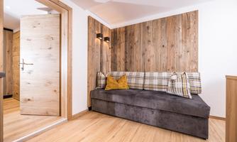 A cozy living area with a dark couch and checkered cushions. The walls are made of light wood and there is a modern entrance.