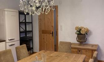 A cozy dining area with a large wooden table and elegant chairs. A sparkling chandelier and a floral decoration create an inviting atmosphere.