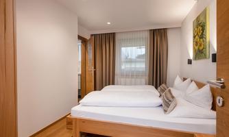 A bright bedroom with two beds and neutral colors. Large windows create a pleasant light atmosphere.