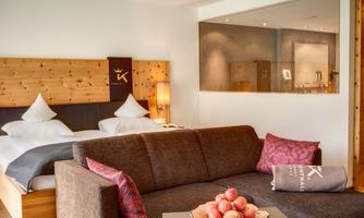 A modern hotel room with a cozy double bed and a seating area. Fresh apples are on the table, and the decor is stylish and inviting.