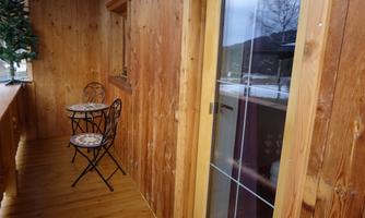 A wooden veranda with a small table and two chairs. The walls are made of wood and there is a glass door.
