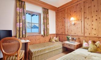 A cozy room with wood paneling and two single beds. The window offers a view of the mountains and the decor is stylishly adorned with floral curtains.