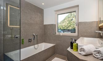 A modern bathroom with a bathtub and a glass shower. A beautiful mountain landscape can be seen through the window.