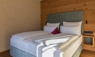 A stylish bedroom with a large double bed and wooden walls. The room is bright and furnished in a modern style.