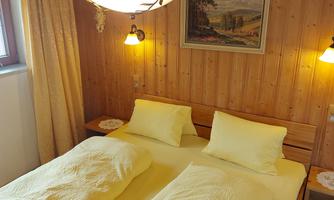 A cozy bedroom with a double bed and yellow bedding. The walls are made of wood and the lighting creates a warm atmosphere.