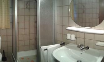 A small bathroom with a shower, sink, and toilet. There is a large mirror and a window with curtains.