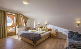 A cozy bedroom with wooden flooring and large windows. The room is bright and modernly furnished, featuring a double bed and a nice view outside.