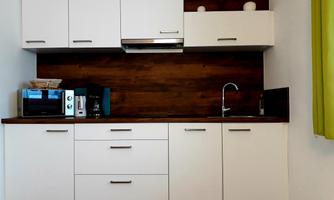 A modern kitchen with white cabinets and a wooden countertop. There is a microwave, a coffee maker, and a faucet.