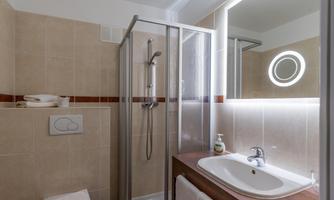 A modern bathroom with a shower and sink. The walls are brightly tiled, and a round mirror provides pleasant light.