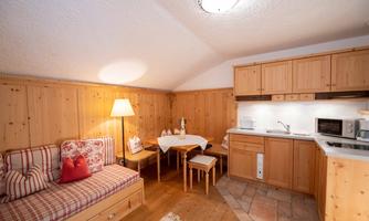 A cozy room with wooden paneling and warm lighting. The furnishings include a small kitchenette, a dining table, and a comfortable seating area.
