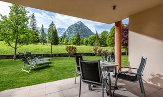 A cozy terrace with chairs and a table, surrounded by well-kept greenery. In the background, a picturesque mountain rises.