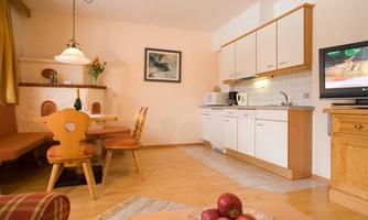 A cozy living space with a modern kitchen and a dining table. Red apples are in the foreground on a table.