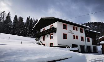 A cozy house in the midst of a snowy landscape. The surroundings are surrounded by fir trees and the sky is cloudy.