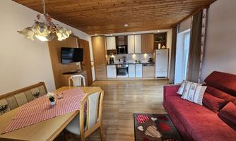A cozy living space with a modern kitchen and a dining area. Red sofas and a rustic wooden floor create an inviting atmosphere.