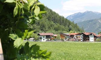 A picturesque landscape with green meadows and huts in the background. The mountains are clearly visible against the sky.