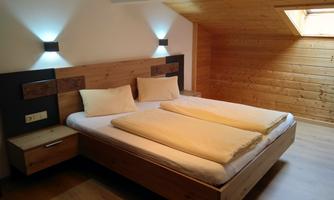 A modern bedroom with a large double bed and wooden paneling. The room features soft lighting and a window under the roof.